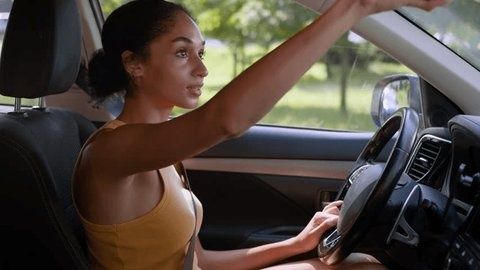 Driver reaching toward the roof while seated behind a car steering wheel