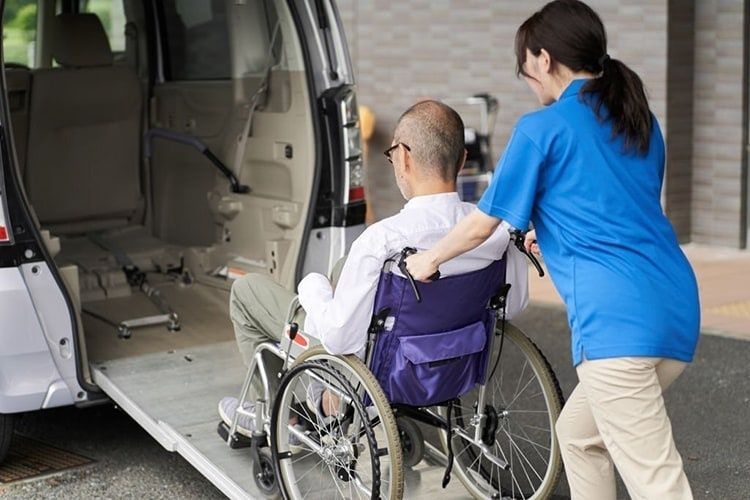 Wheelchair user assisted toward an accessible vehicle with a ramp